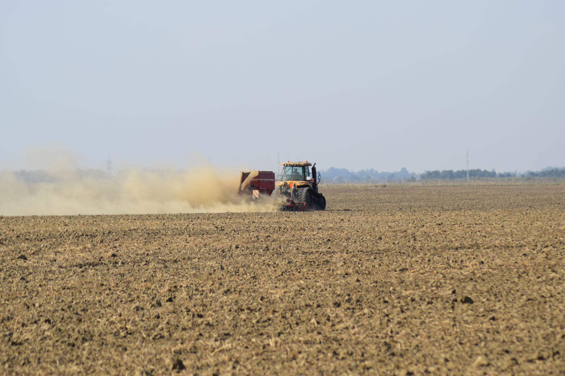 Tractor con implemento de siembra trabajando el suelo levantando polvo en un día soleado